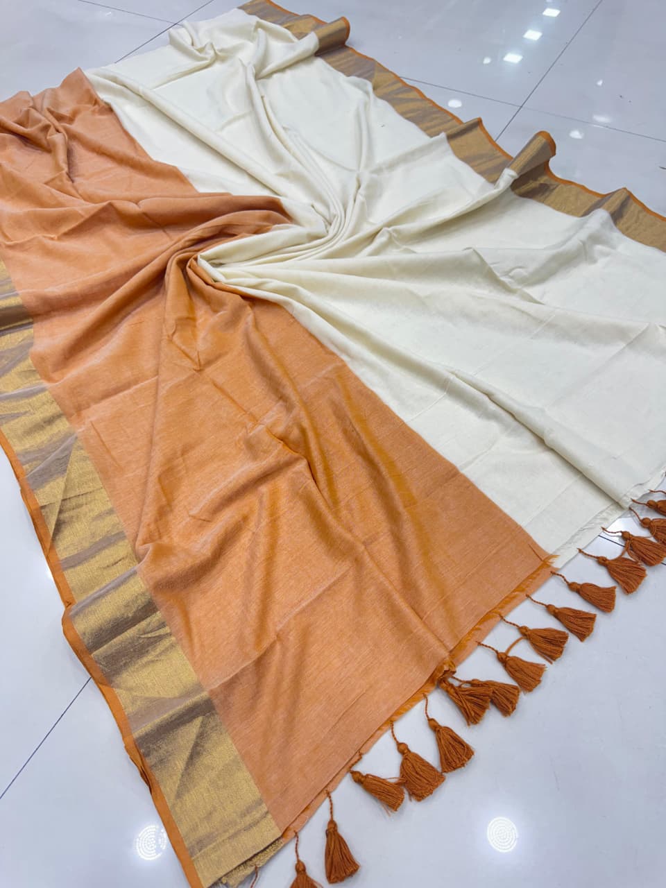 Rust Orange and cream panels with an olive-green border and blue-and-white tassel detailing on the pallu.